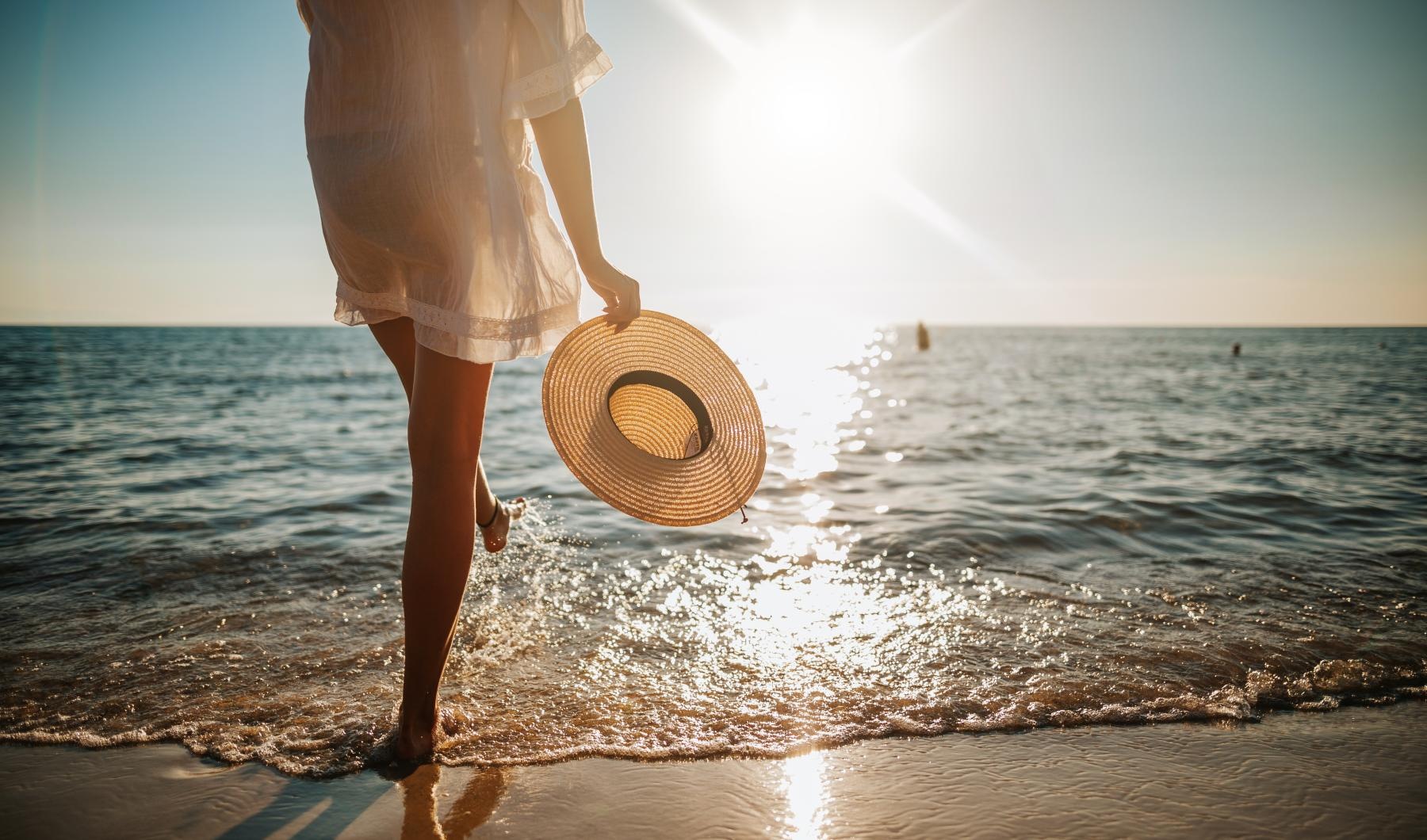 a woman holding a hat on a beach
